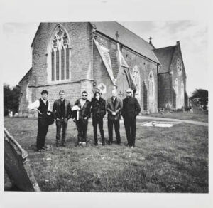 LP Hülle vorne, Let England Shake. Foto der Band vor einer Kirche in Dorset, England.